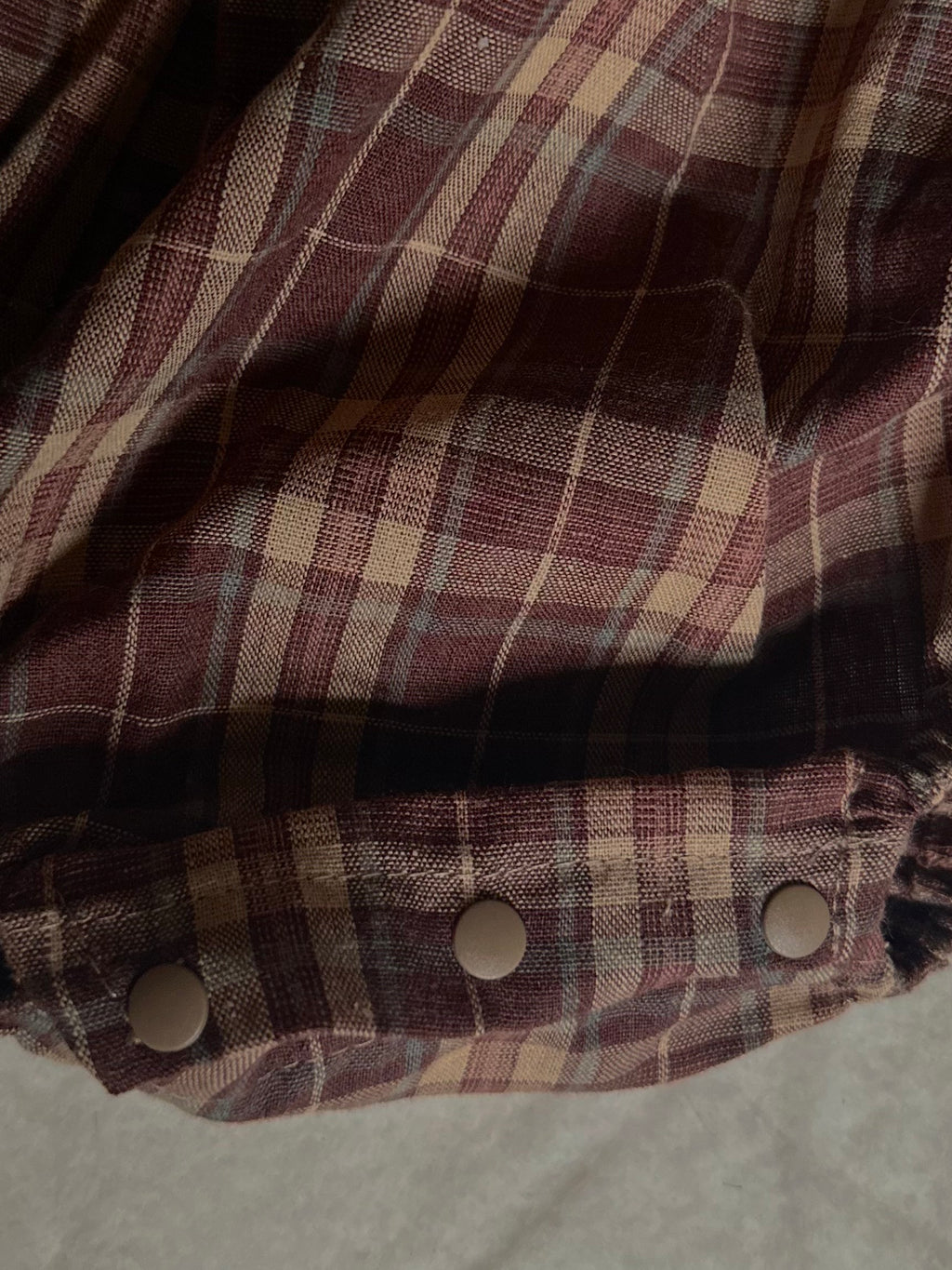 Details of snap button enclosure at bottom of 100% cotton Brownish plaid bubble romper with lace front and collar. 