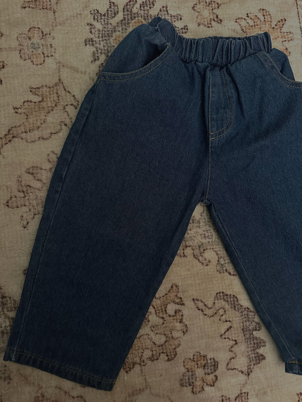 100% cotton medium to dark wash denim jeans laid out on rug. 