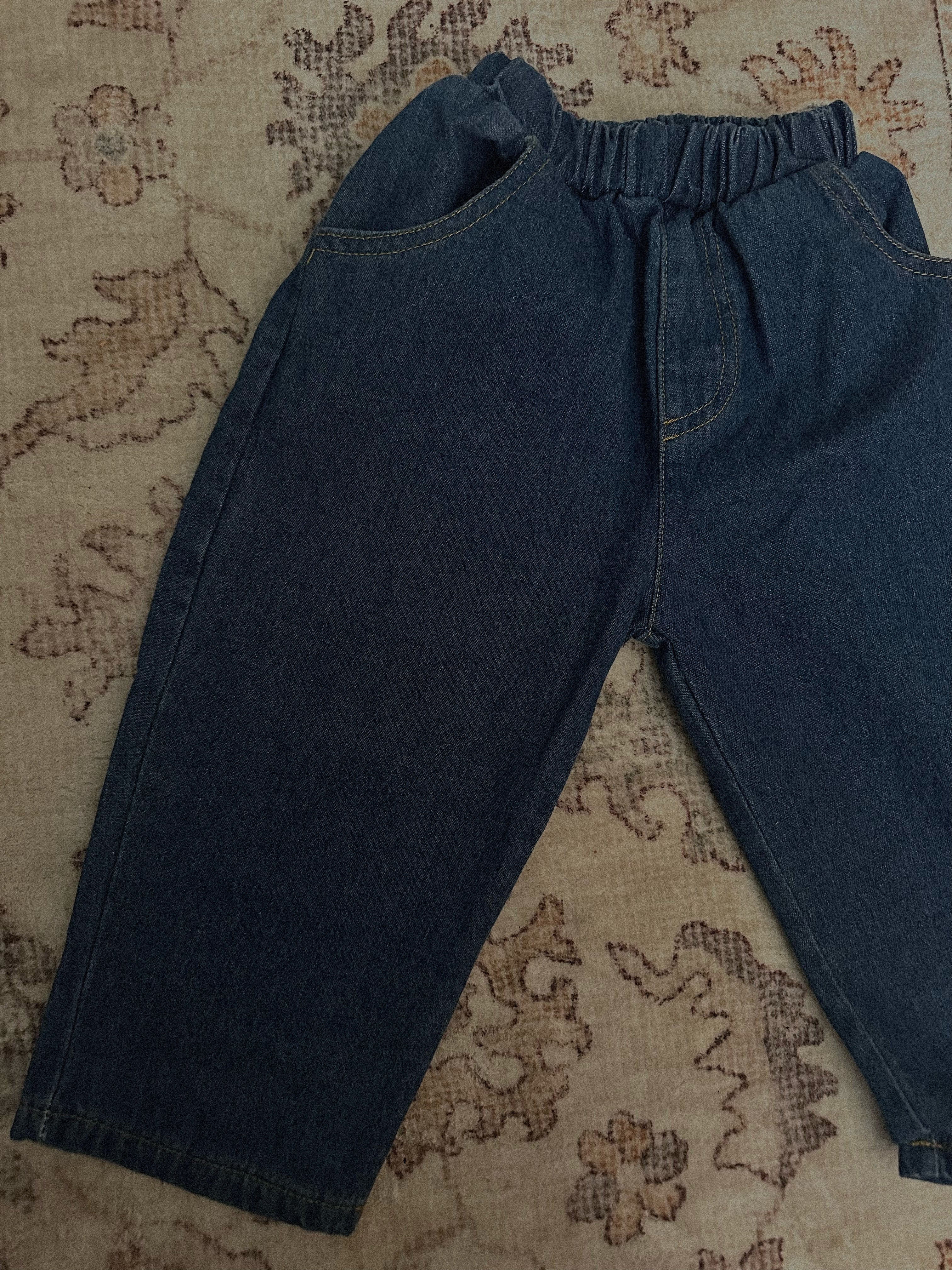 100% cotton medium to dark wash denim jeans laid out on rug. 