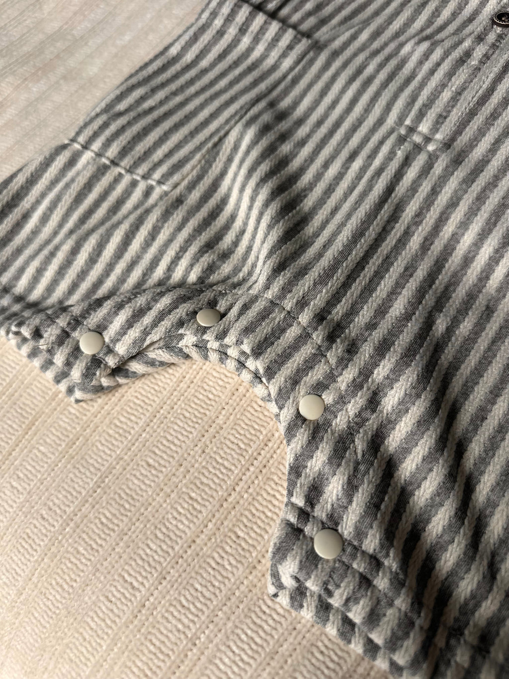Close-up of buttons on a blue grat and white striped cotton baby boy romper with buttons on a beige surface