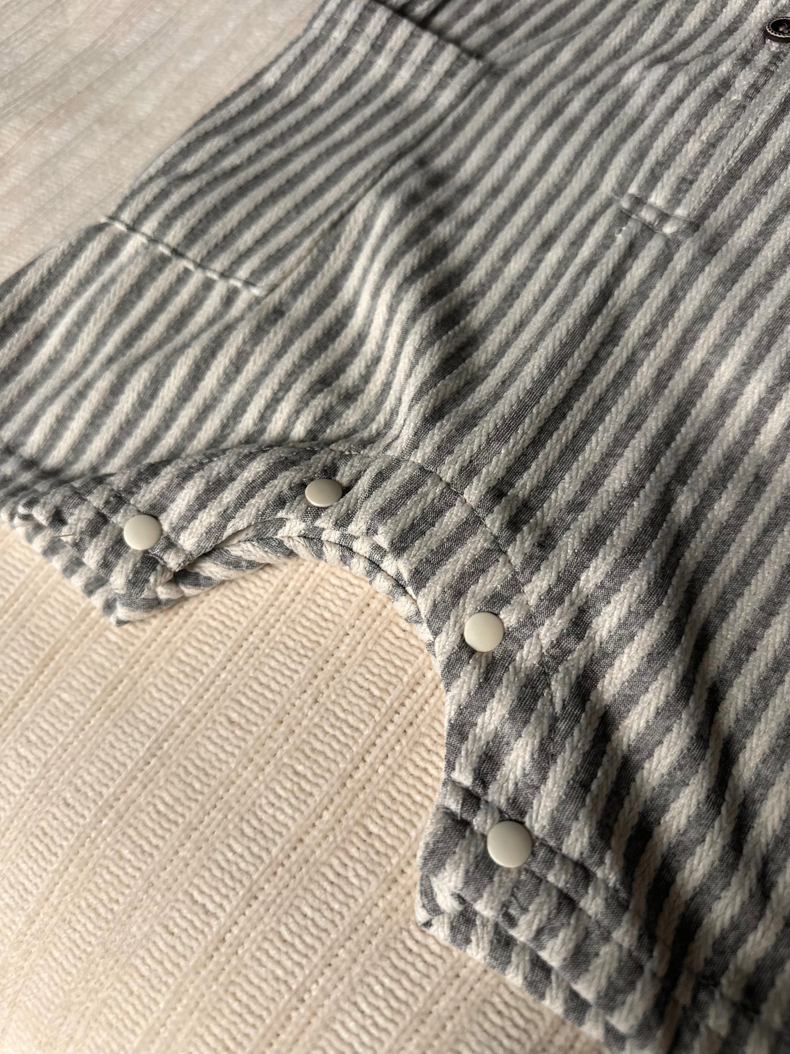 Close-up of buttons on a blue grat and white striped cotton baby boy romper with buttons on a beige surface
