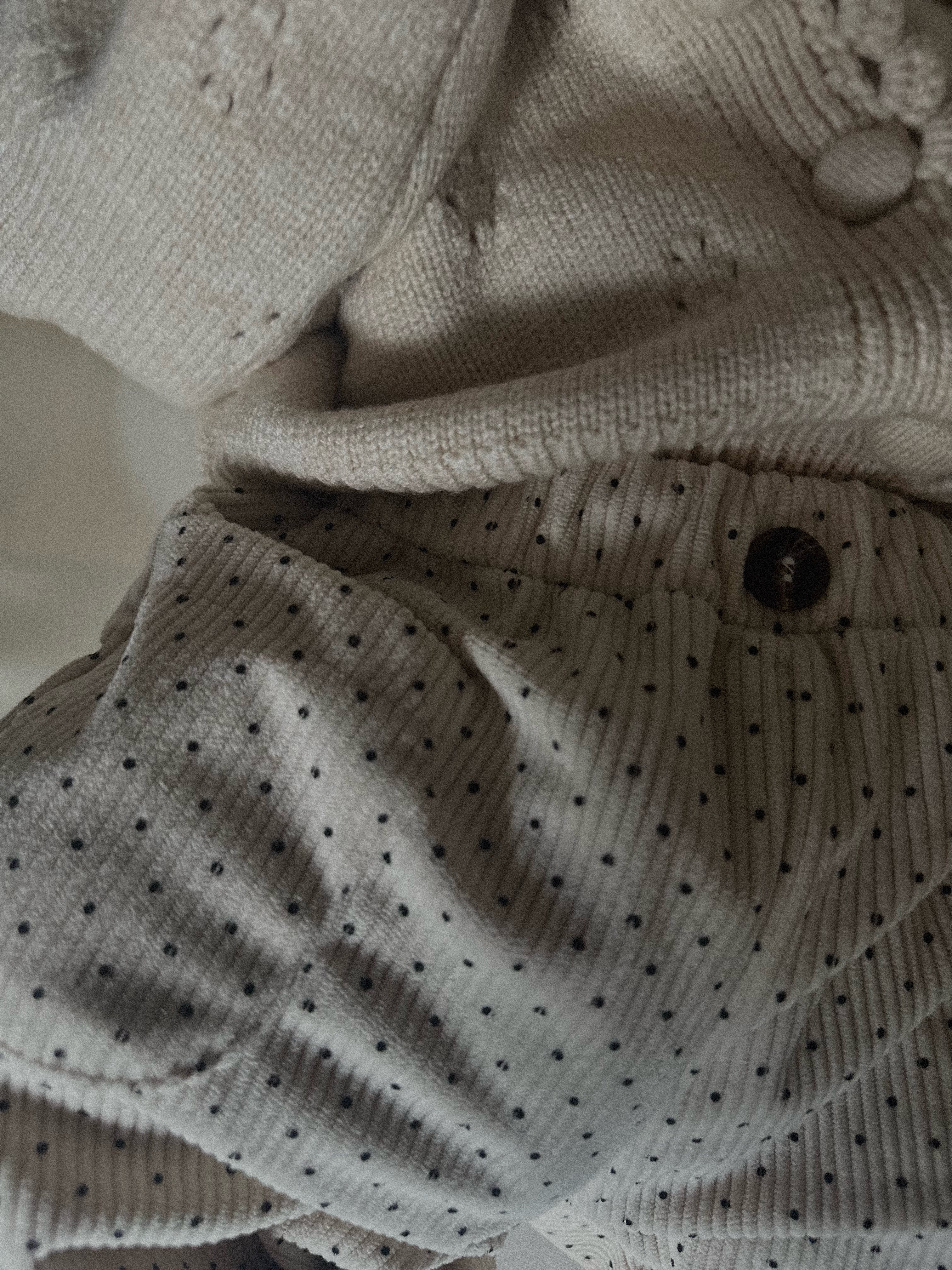 Baby wearing Light cream colored soft polka dot corduroy pants with button. 
