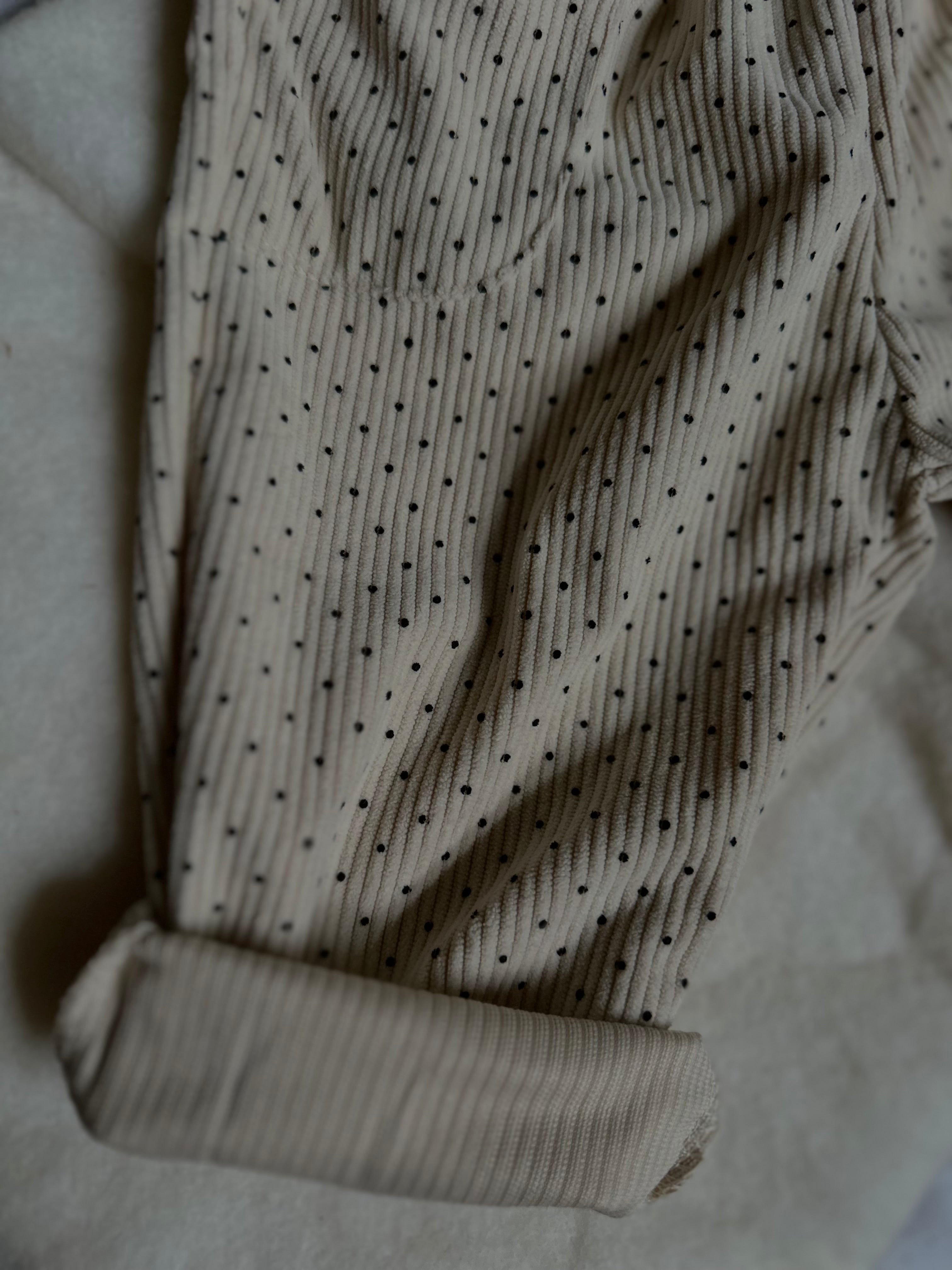 Cuffed hem of Light cream colored soft polka dot corduroy pants with button. 