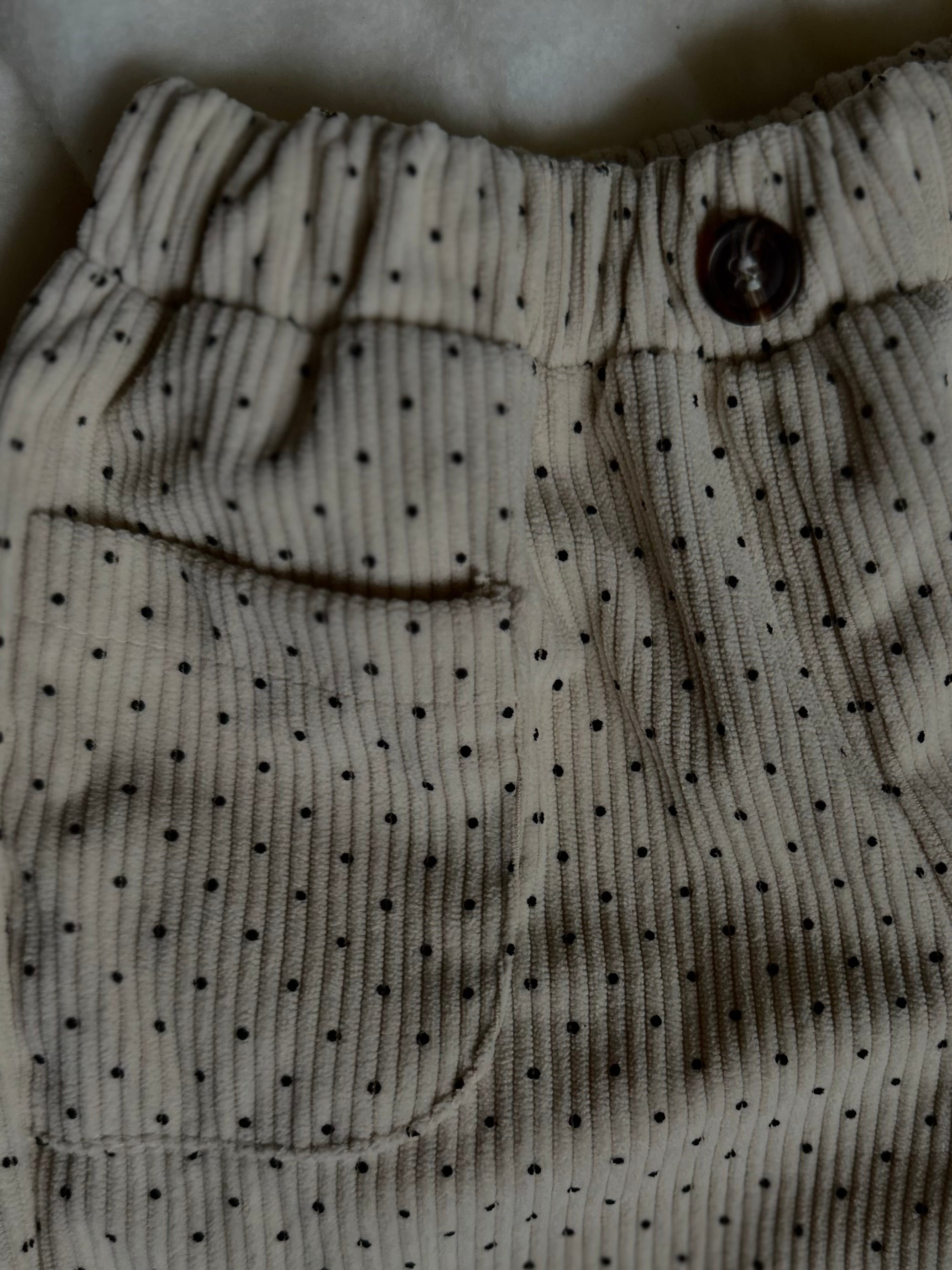 Detail of top and button of Light cream colored soft polka dot corduroy pants with button. 