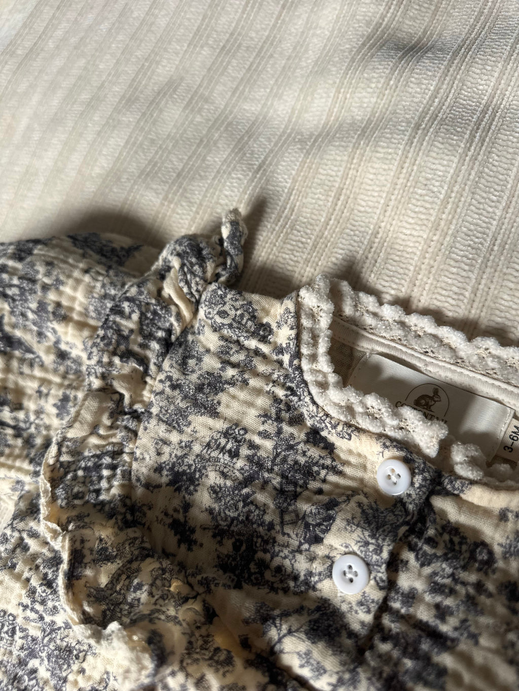 Close-up of blue gray floral-patterned baby romper with buttons on a textured surface