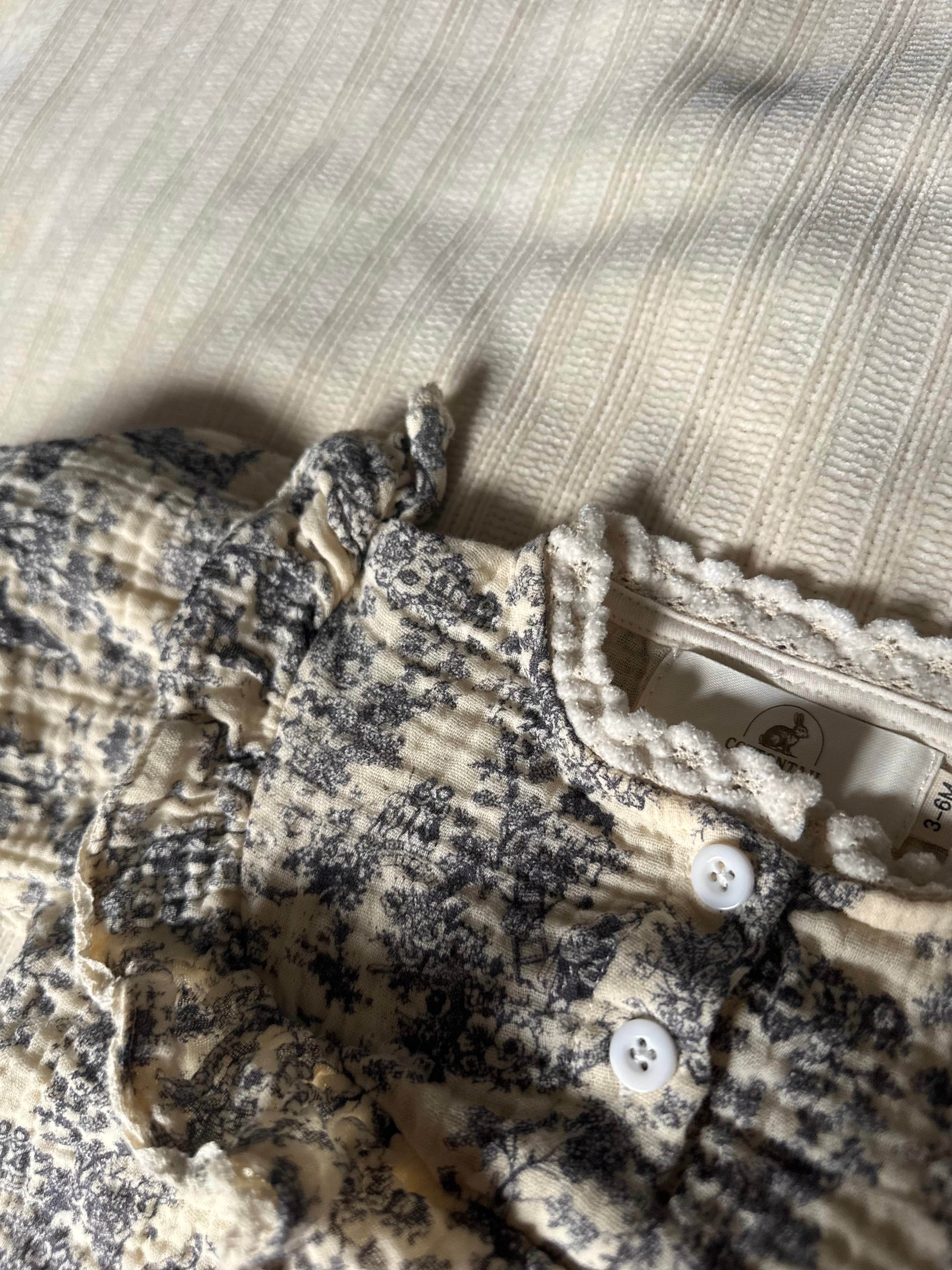 Close-up of blue gray floral-patterned baby romper with buttons on a textured surface